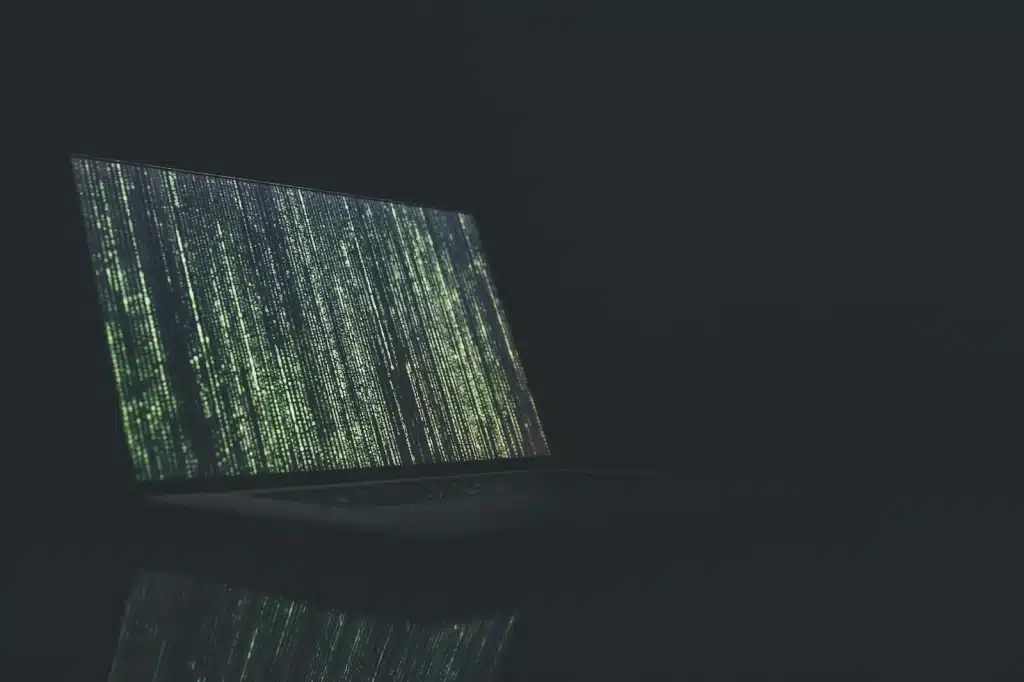 Laptop deschis în întuneric, cu linii de cod verde pe ecran